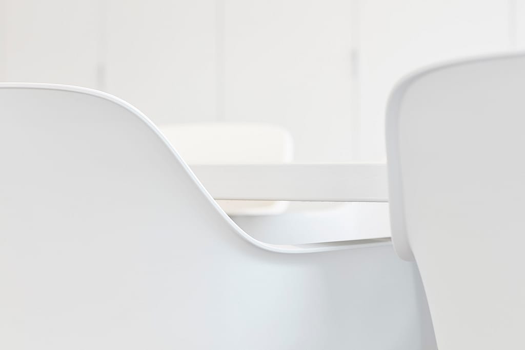 Minimale Nahaufnahme weißer Kapitänsstühle um einen weißen Tisch, wobei die glatten, geschwungenen Linien der Sitzgelegenheiten hervorgehoben werden.