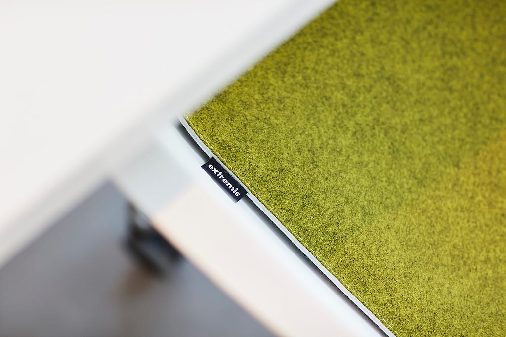 Nahaufnahme eines grünen Schreibtischaccessoires aus Filz mit einem kleinen Extremis-Etikett, das auf dem weißen Bürotisch ruht.