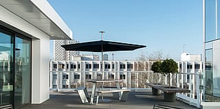 Weißer Anker-Picknicktisch unter einem dunklen Inumbrina-Sonnenschirm auf einer geräumigen Dachterrasse mit einer modernen weißen Gebäudefassade und der Skyline von Rennes im Hintergrund.