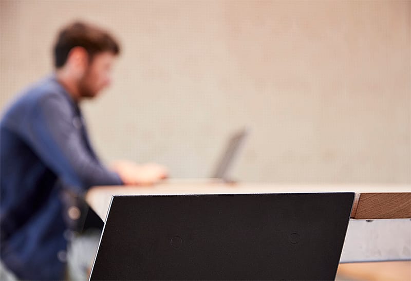 Intérieur de coworking avec de longues lignes de visibilité, des fermes de toit exposées et des tables communes conçues pour les réunions avec les clients, le travail sur ordinateur portable et les conversations rapides.