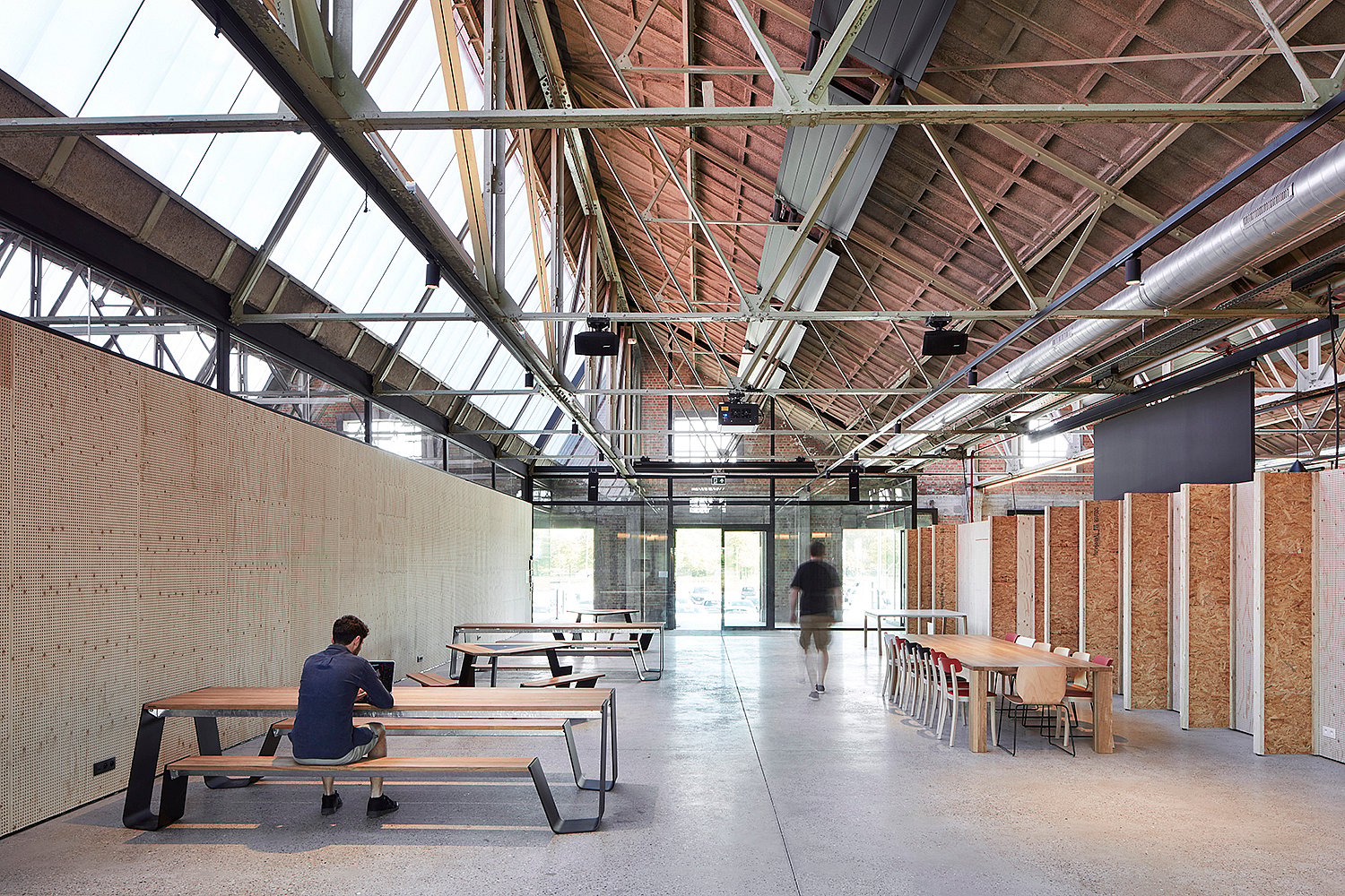 Table de pique-nique Communal Hopper avec des pieds en métal foncé et un dessus en bois dur, positionné dans l’intérieur lumineux du bureau industriel.