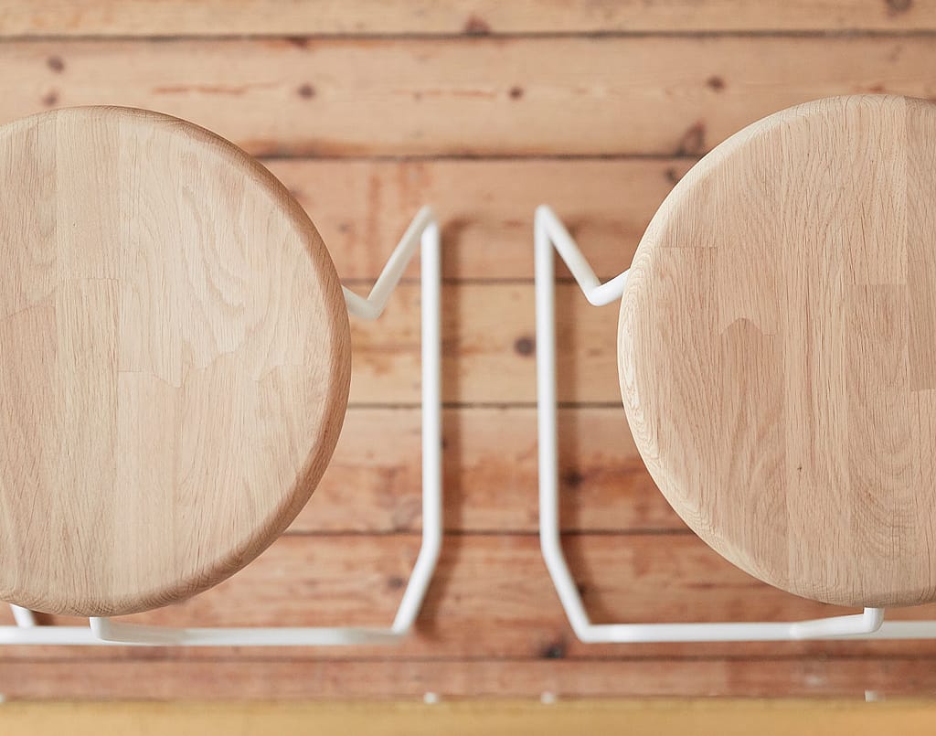 Tiki bar stool detail showing the oak seat and integrated foot support, positioned against the tiled base of the bar.