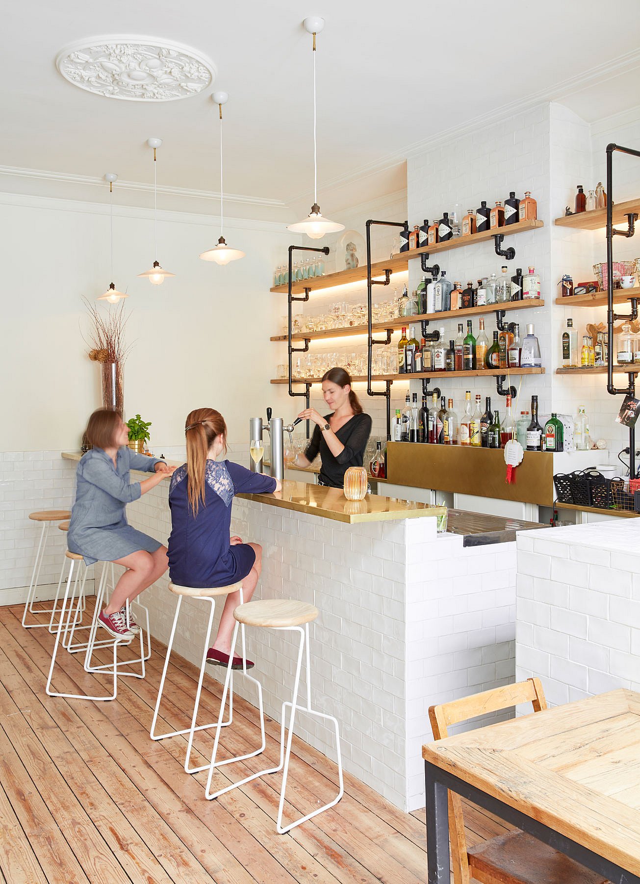 Intérieur élégant du bar historique Den Olifant, avec des tabourets de bar Tiki alignés autour d'un comptoir en laiton, encadré d'étagères en bois ouvertes, de carreaux blancs brillants et d'un chaleureux parquet.