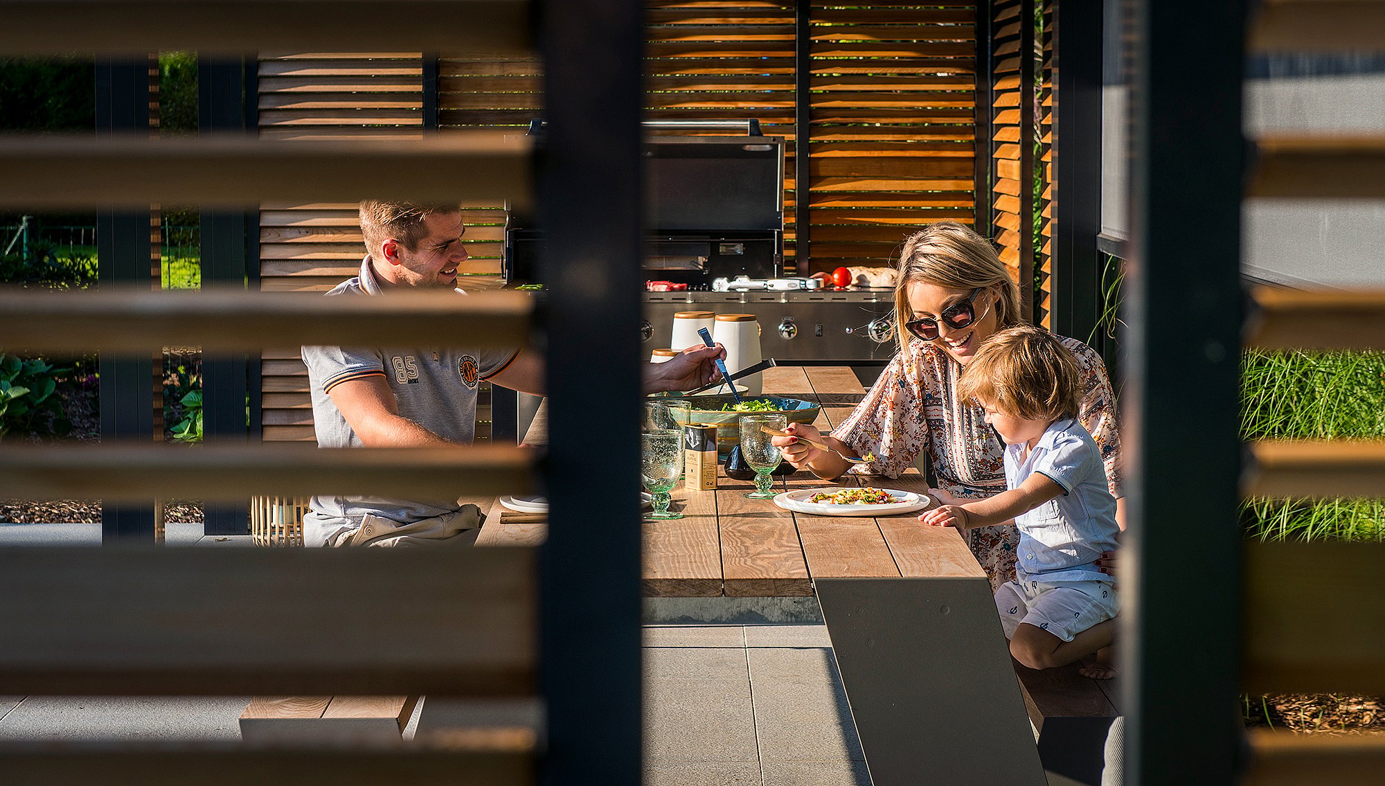 Hopper-Tisch unter einer Lattenpergola neben dem Pool, gestaltet als Außenraum für alltägliche Aktivitäten in einer ruhigen Wohngartenumgebung.