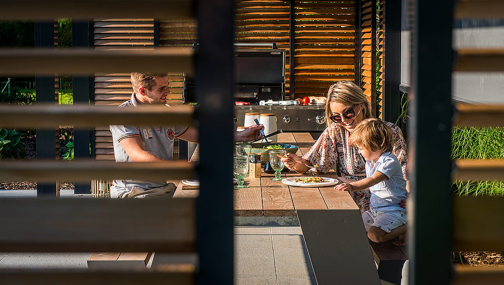 Hopper-Tisch unter einer Lattenpergola neben dem Pool, gestaltet als Außenraum für alltägliche Aktivitäten in einer ruhigen Wohngartenumgebung.