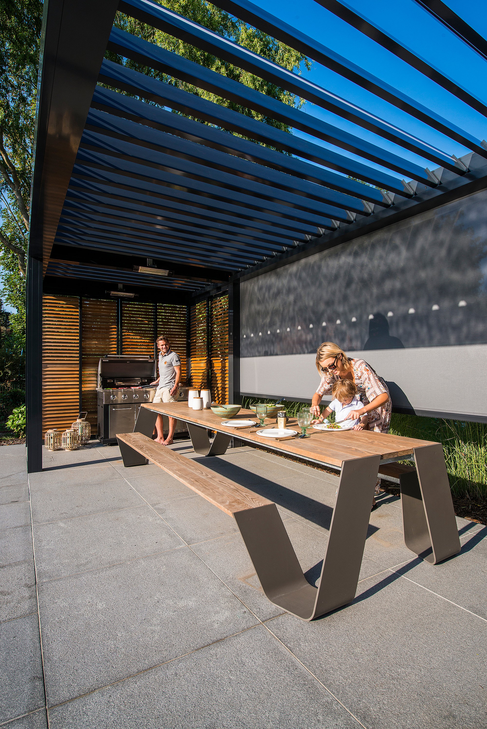 Geschützter Ess- und Arbeitsbereich im Freien mit einem Hopper-Tisch unter einer modernen Pergola, der den Komfort eines Innenraums mit einer Open-Air-Poolterrasse verbindet