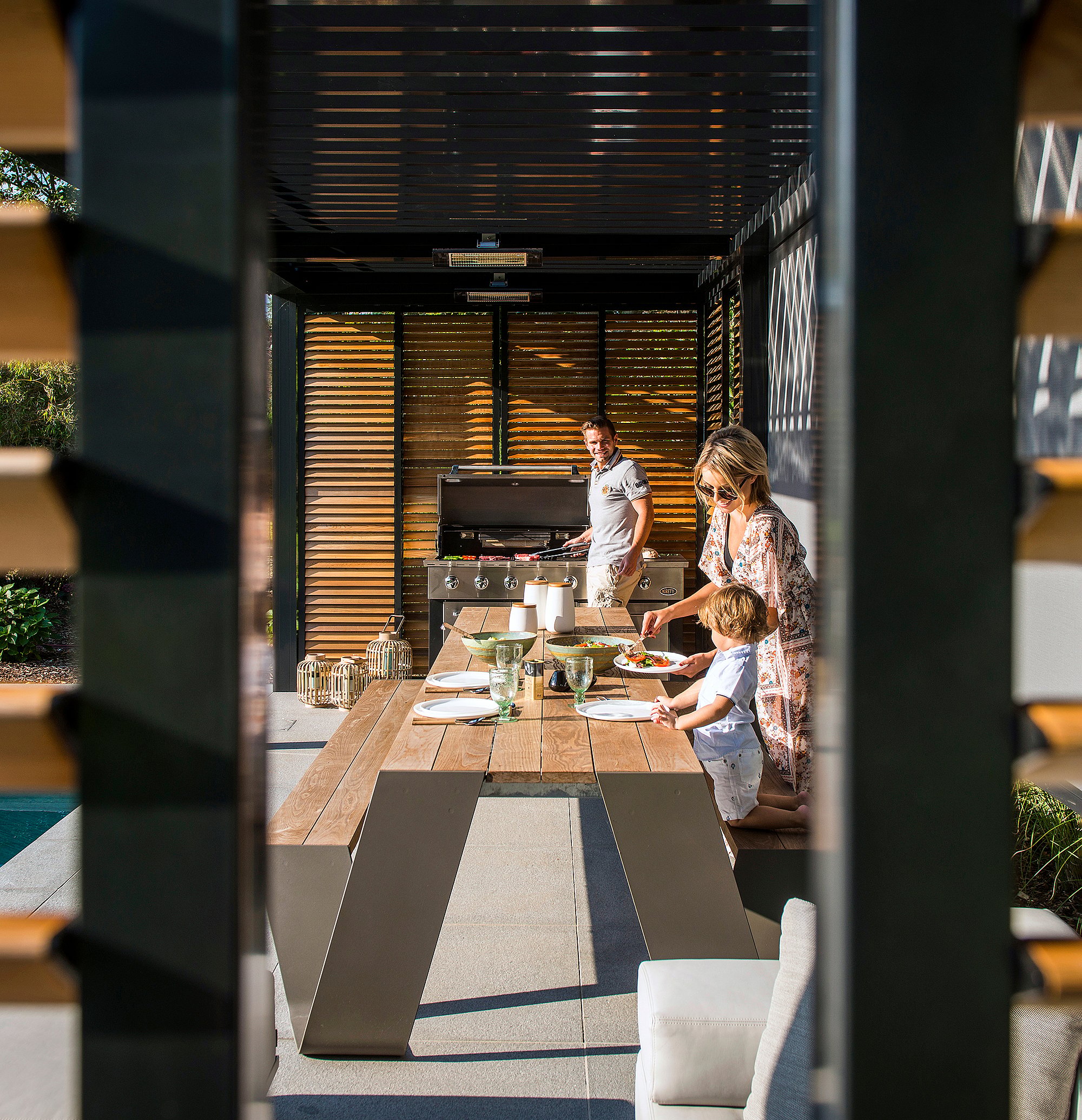 Hopper-Tisch am Pool unter einer modernen Pergola mit warmen Holzlatten, der einen luxuriösen Ort zum Kochen, Essen, Lesen oder Ausruhen im Freien bietet.