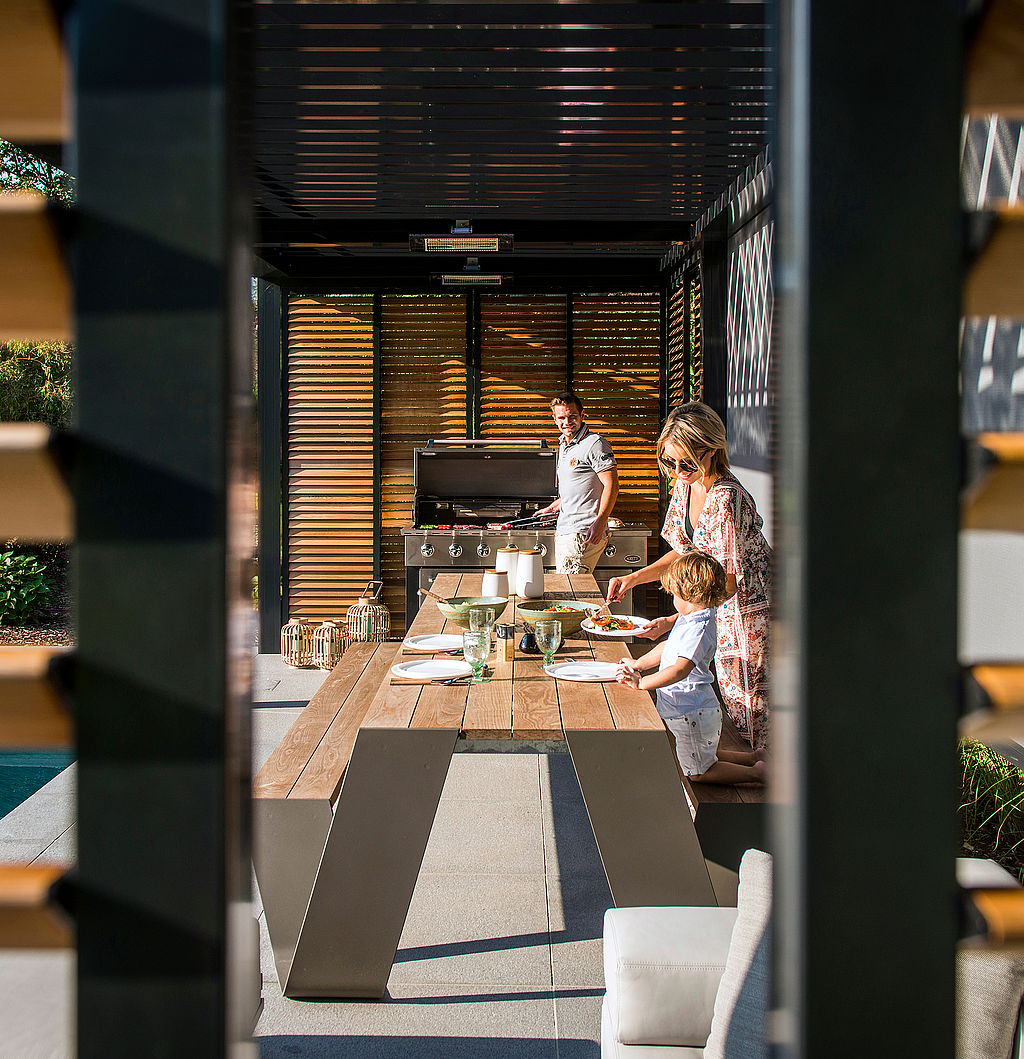 Hopper-Tisch am Pool unter einer modernen Pergola mit warmen Holzlatten, der einen luxuriösen Ort zum Kochen, Essen, Lesen oder Ausruhen im Freien bietet.