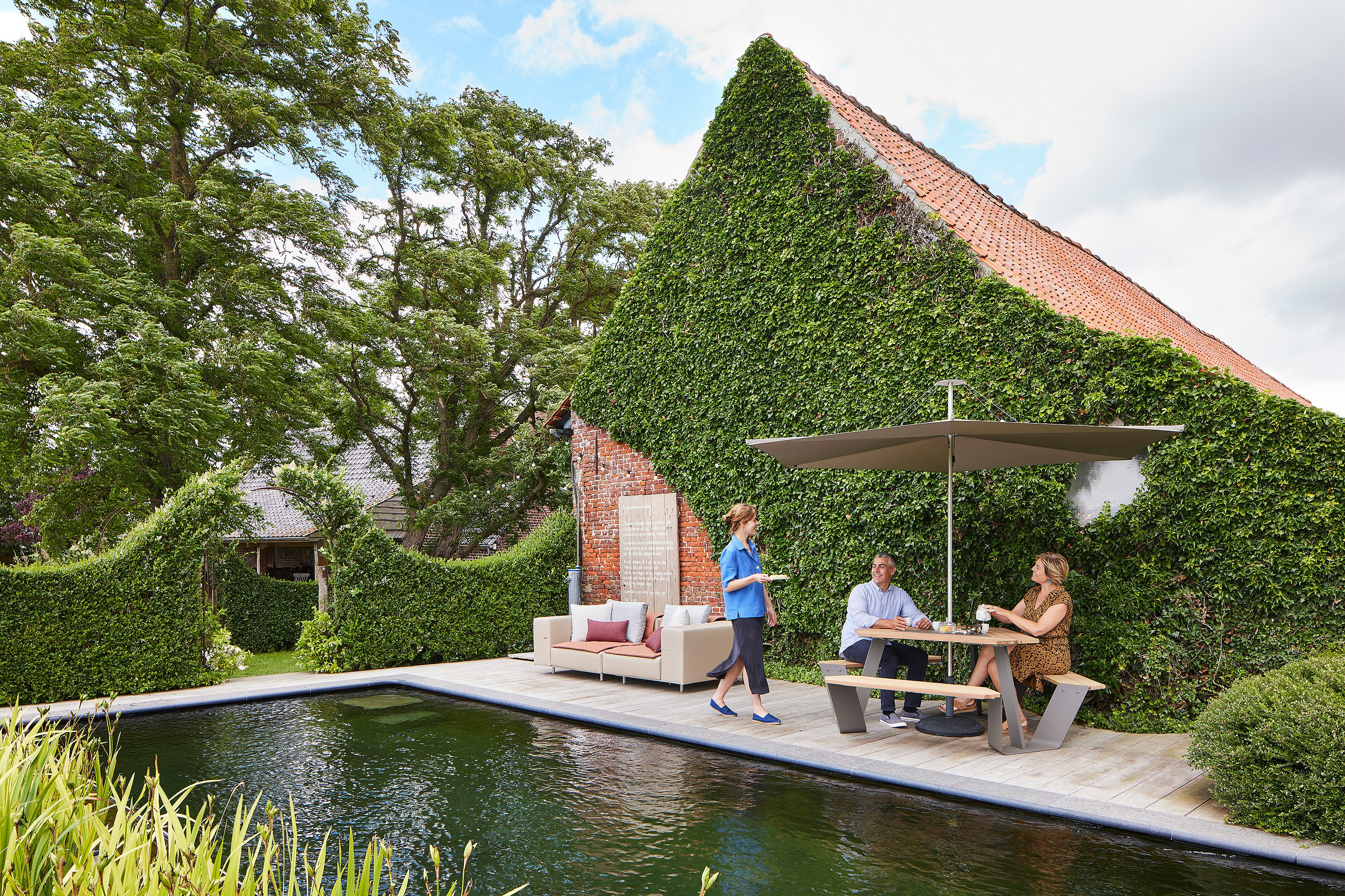 Charming cottage garden at a rural guesthouse in the Belgian countryside, with multiple outdoor seating areas creating a peaceful, inviting place to relax.