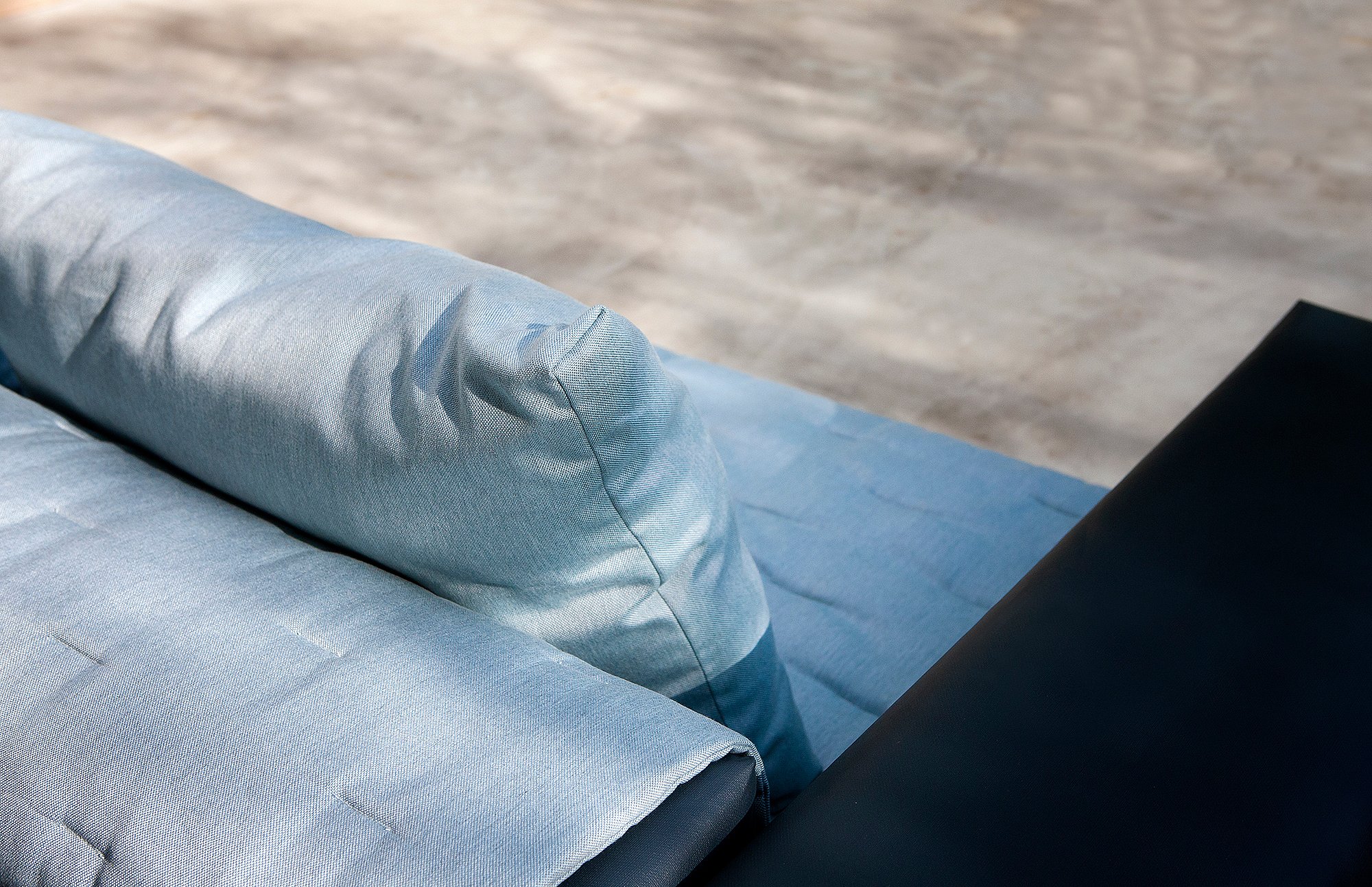 Top view of the Walrus sofa corner with quilted pale blue cushions and a cylindrical backrest against the dark frame.