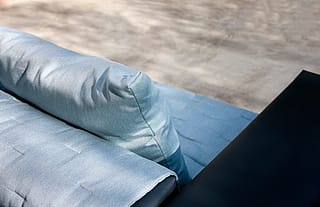 Top view of the Walrus sofa corner with quilted pale blue cushions and a cylindrical backrest against the dark frame.