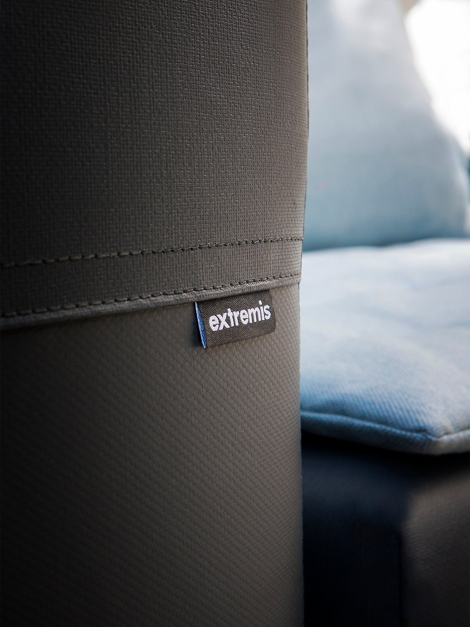 “Close-up of the textured dark gray side of the Walrus sofa with an Extremis label, with a pale blue cushion softly blurred in the background.