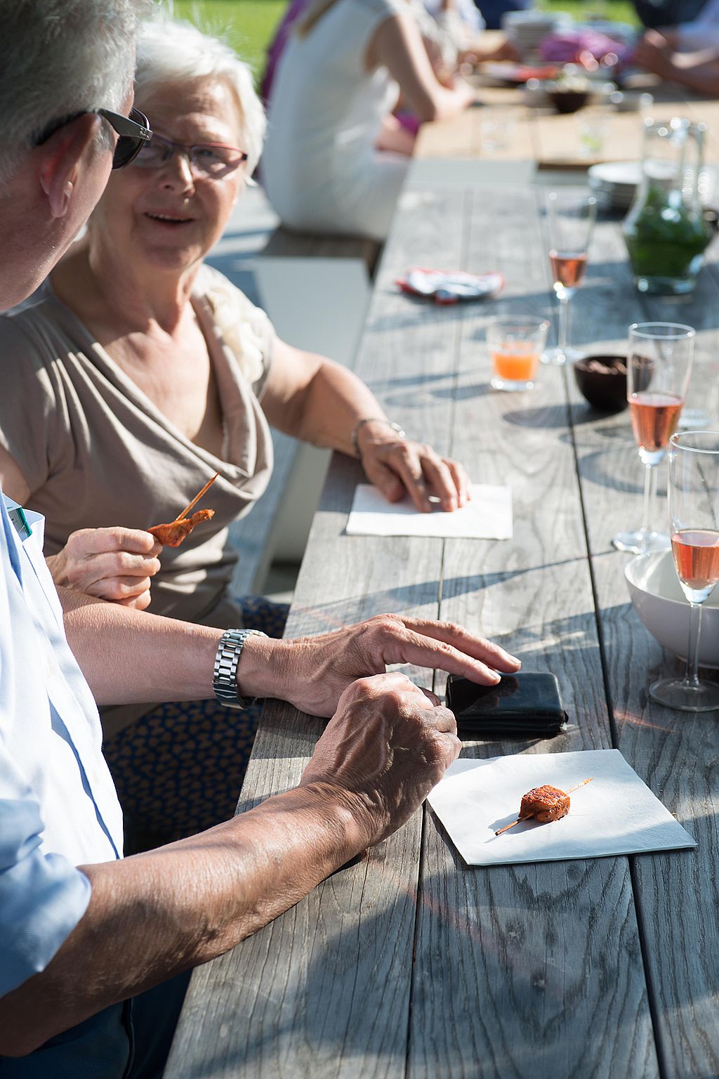 Older couple sitting together at a weathered Hopper tabletop with drinks and appetizers, highlighting the shared bench and relaxed conversation.