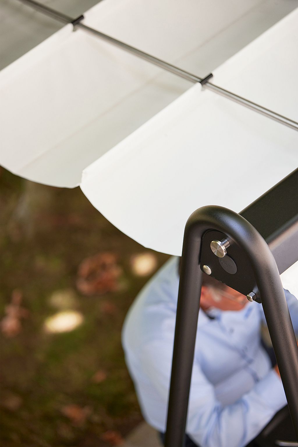 Close-up van het zwarte AMAi-frame en de witte stoffen luifel, met de nadruk op de gebogen ondersteuning en bevestigingsdetails van het buitenkapsysteem.