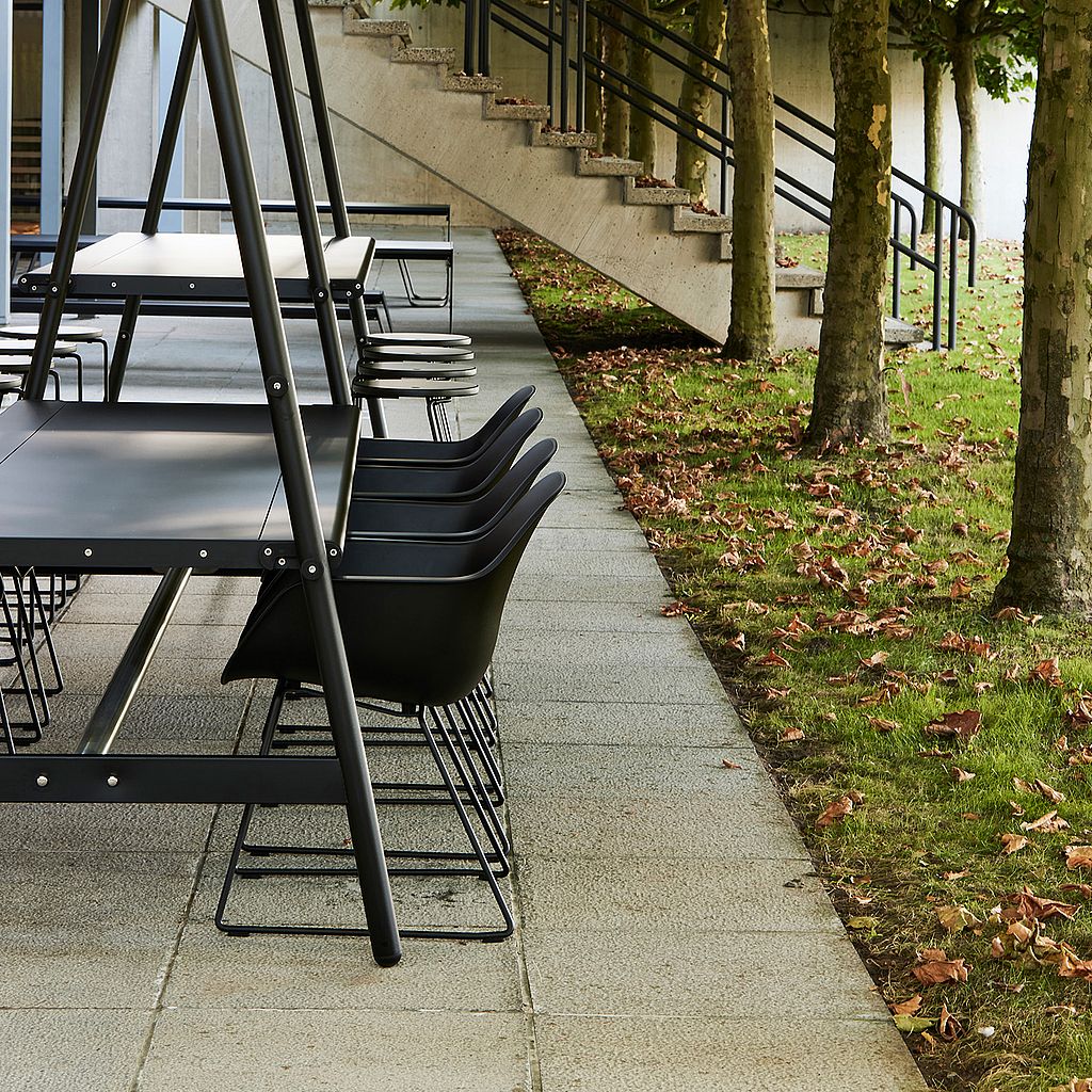 Black Captain's Pipe Chairs at a dark grey table beneath a canvas canopy on a paved terrace lined with trees.