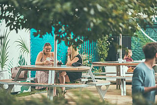 Deux femmes assises à un gargantua sur une terrasse en bois, ombragée par une grande inumbra blanche dans la cour du bar d’été.