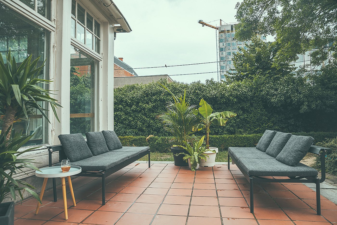 Deux canapés de salon extérieur sombres se faisant face sur une véranda en terre cuite, avec des plantes en pot et une petite table ronde entre les coins salons.