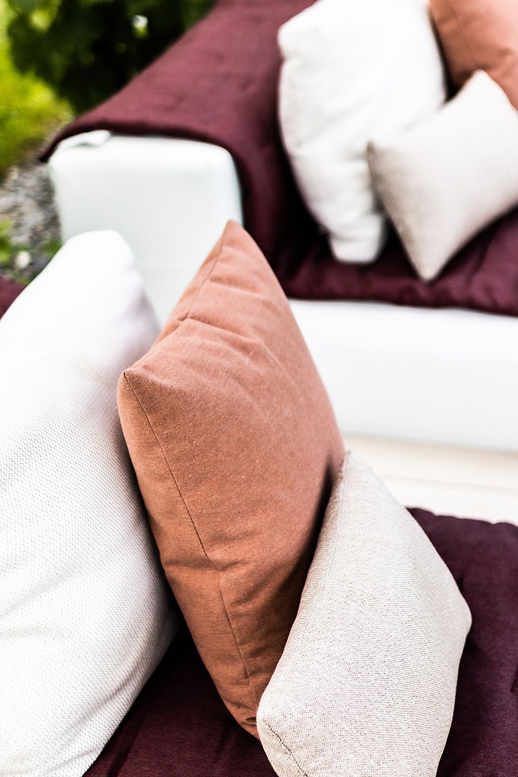Close-up of soft outdoor cushions in dusty pink, off-white, and deep burgundy tones arranged on a modular lounge sofa.
