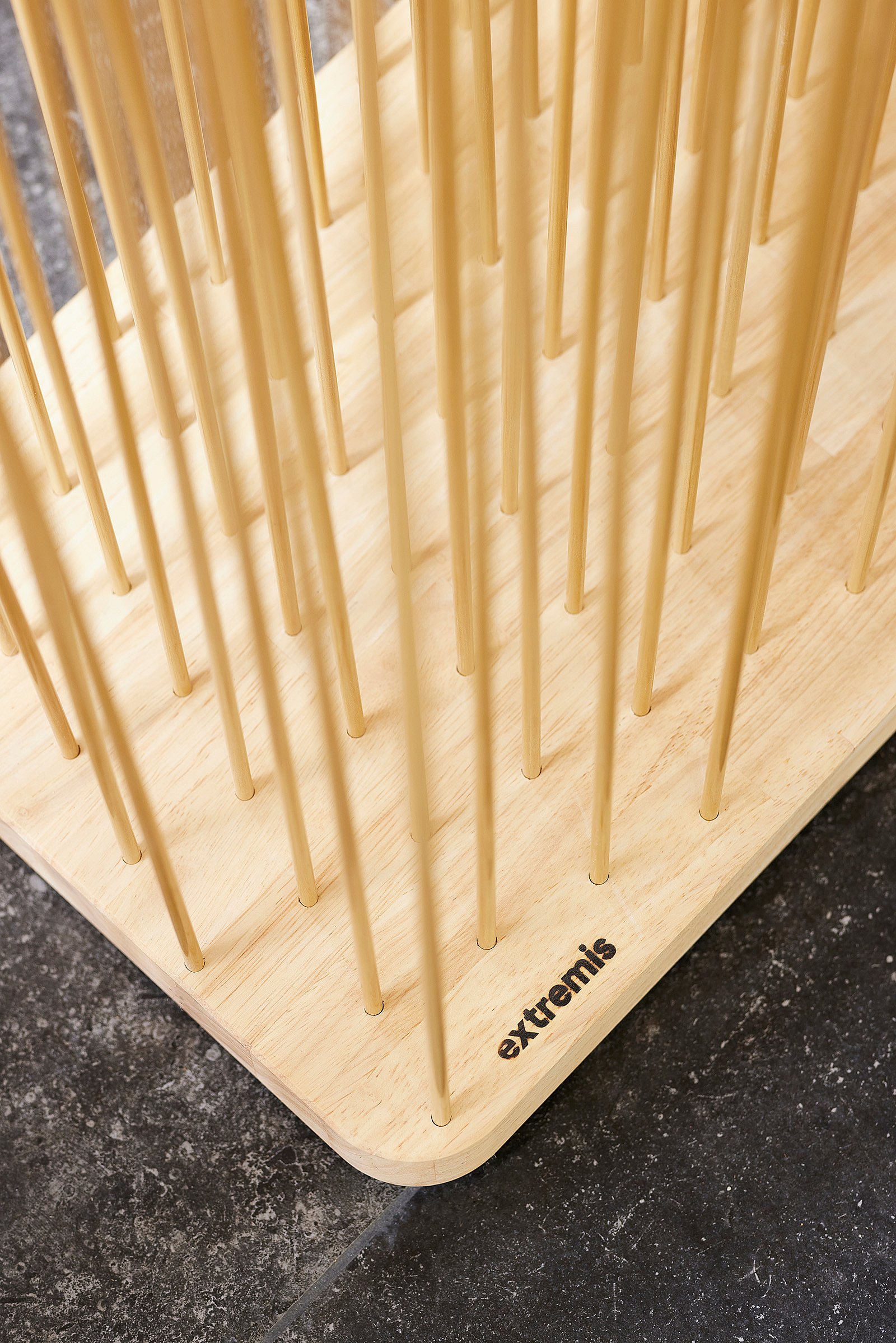 Close-up van de basis van een houtkleurige Sticks kamerverdeler, met slanke verticale staven bevestigd in een licht houten platform met het Extremis-logo op de hoek gedrukt.