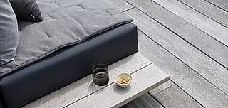 Close-up van de houten zijplank van een Walrus-buitenbank met een donker glas en een kleine kom pinda's op een bleek houten dek.