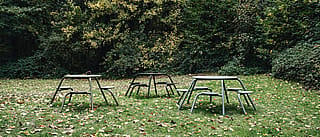 Das historische Steinschloss Warande mit seinen Türmchen und hohen Fenstern, im Hintergrund mehrere grüne und schwarze Virus-Picknicktische, die an einem trüben Herbsttag über einen Kiesweg und eine laubbedeckte Wiese verteilt sind. Drei Virus-Picknicktische in gedeckten Grün- und Schwarztönen stehen auf einer grasbewachsenen Lichtung, bedeckt mit Laub, im Hintergrund ein dichtes, dunkles Waldstück.