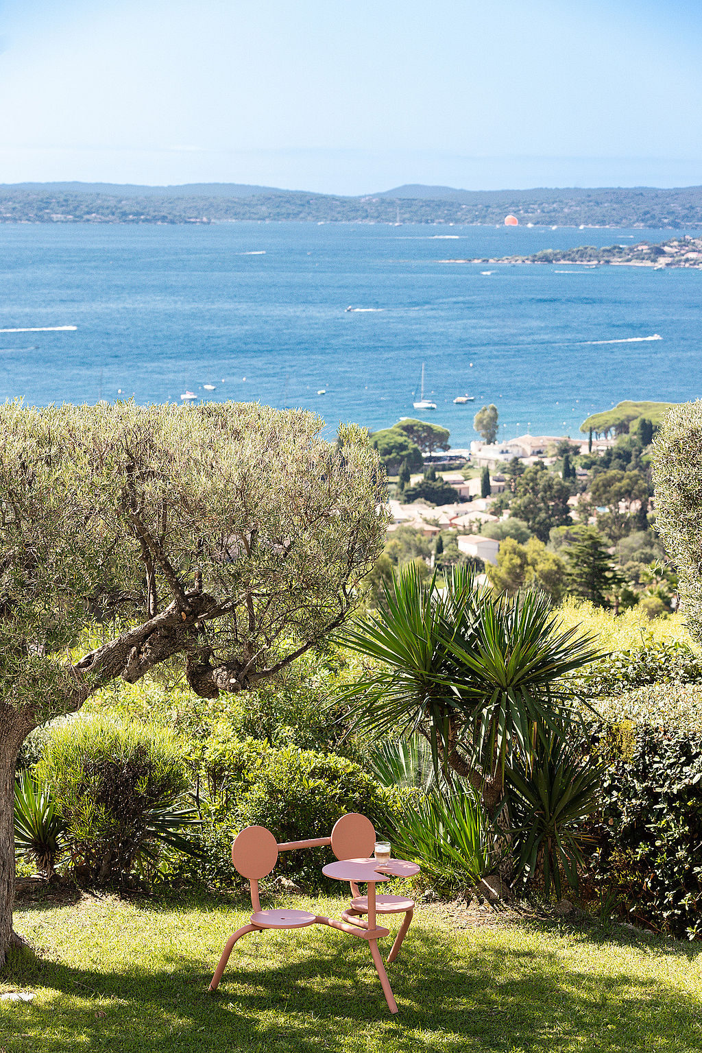 Bistroo rose placé sur une pelouse herbeuse sous les arbres, avec une vue panoramique sur la mer en arrière-plan.
