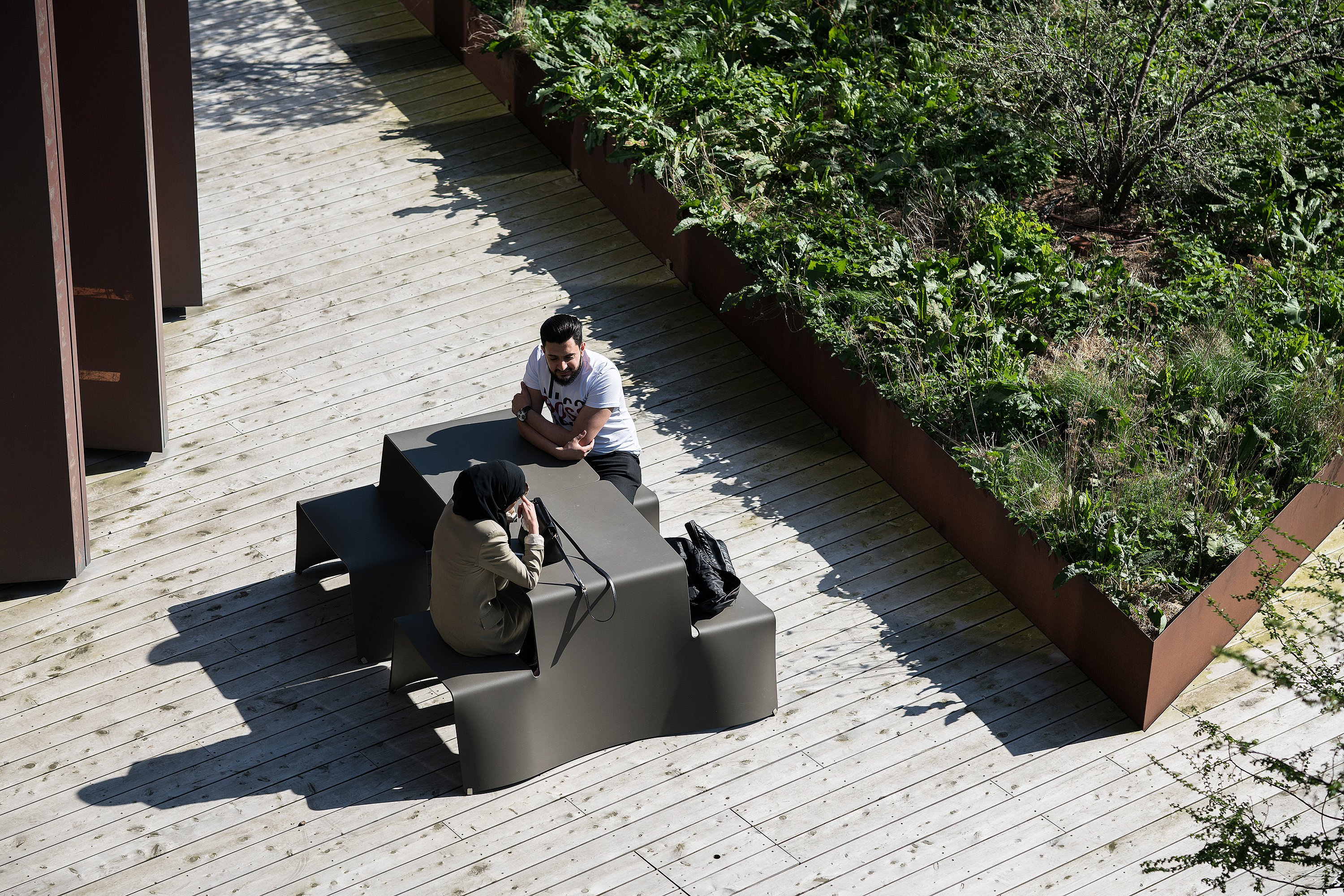 People sitting at picnik tables along a broad paved path through the landscaped park, with the modern campus buildings behind them.