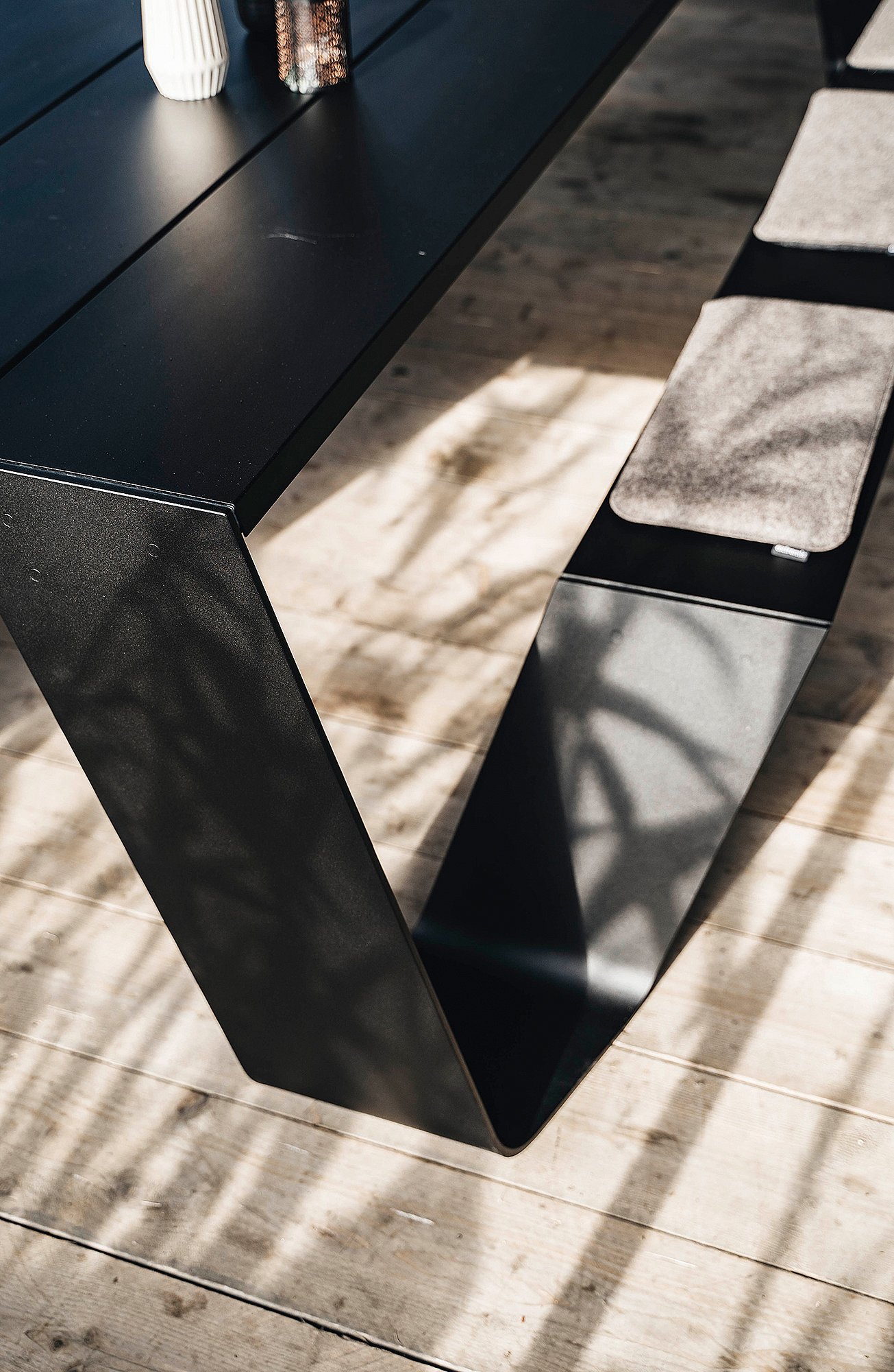 Close-up of the black Hopper table leg and matching bench on a wooden floor, with soft shadows cast across the surface.