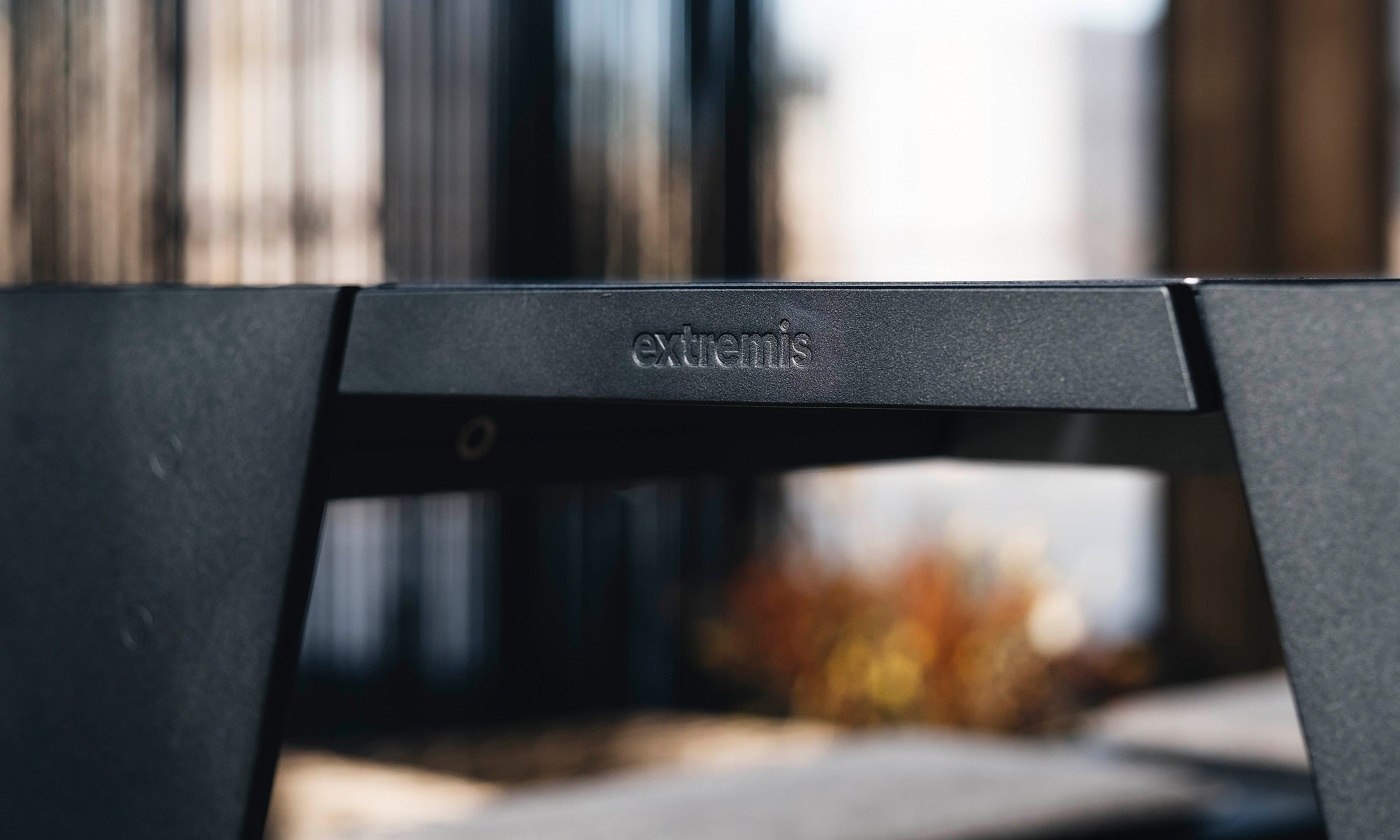 Close-up of the Extremis logo embossed on the black metal frame of the table, with the bench and interior softly blurred in the background.