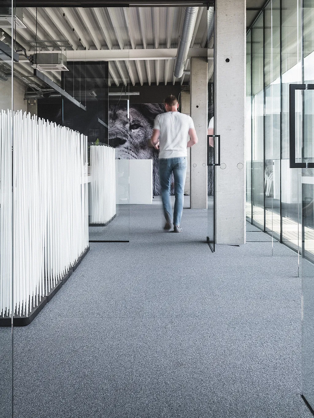 Witte Sticks kamerverdeler naast een rij witte bureaus in een lichte industriële kantoorgang, met een persoon die langs glazen vergaderruimten loopt.