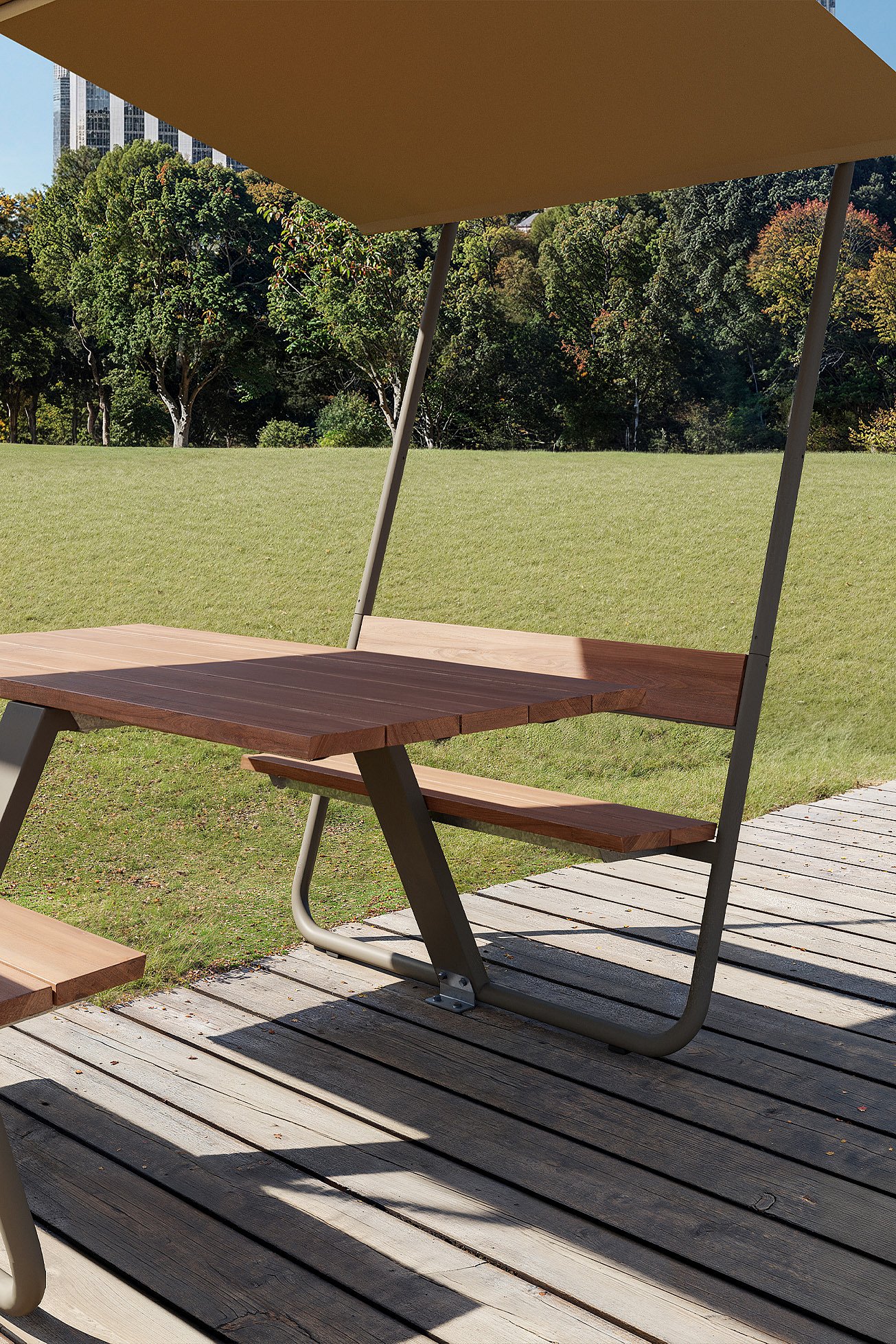 Terracotta-colored Manille picnic table with integrated benches and a fixed roof shade, standing on a gravel path in front of trees and a city skyline.