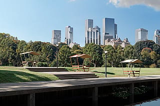 Close-up of a Manille picnic table with wooden tabletop and benches beneath a fixed roof shade, anchored to a timber deck beside an open grassy lawn.