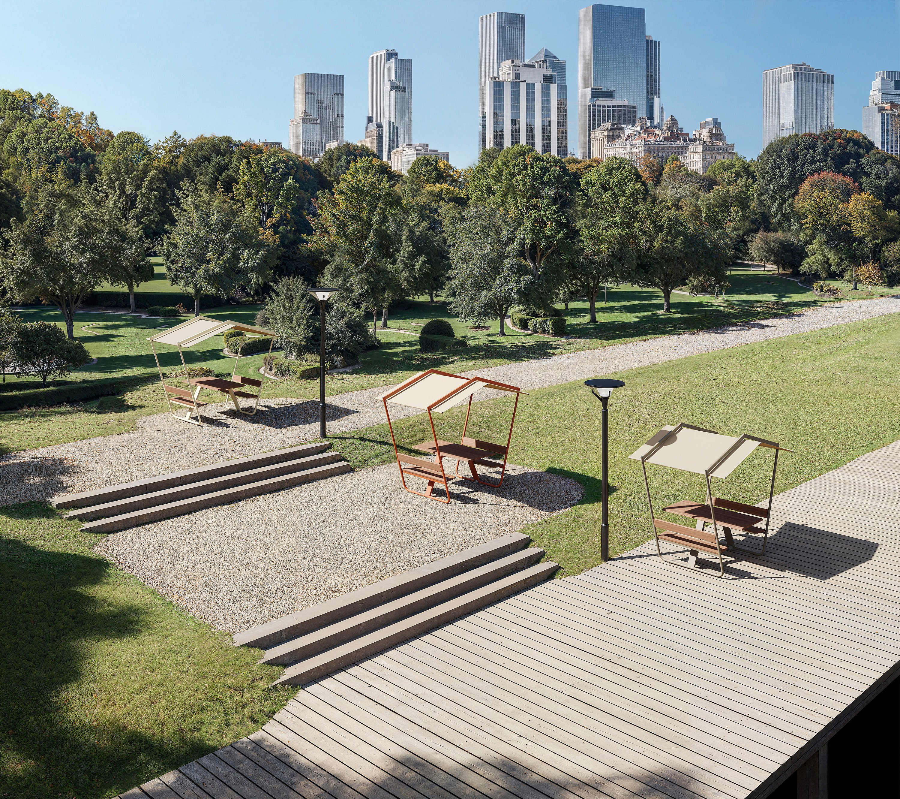 Drei Manille-Picknicktische mit festen Dachschirmen, die über einen angelegten Stadtpark verteilt sind, mit Stufen, Laternenpfählen, einer Holzpromenade über dem Wasser und einer modernen Skyline, die sich hinter den Bäumen erhebt.
