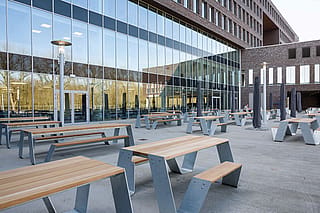 Une autre vue de la terrasse moderne de l’hôpital avec plusieurs tables de pique-nique Hopper disposées dans un espace extérieur ouvert et accessible à côté du bâtiment vitré.