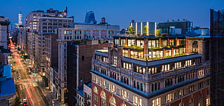 Abendlicher Stadtblick auf das beleuchtete Dachgebäude des Mastercard Tech Hub mit mehreren bepflanzten Terrassen und Sitzgelegenheiten im Freien über einer belebten Straße in Manhattan.