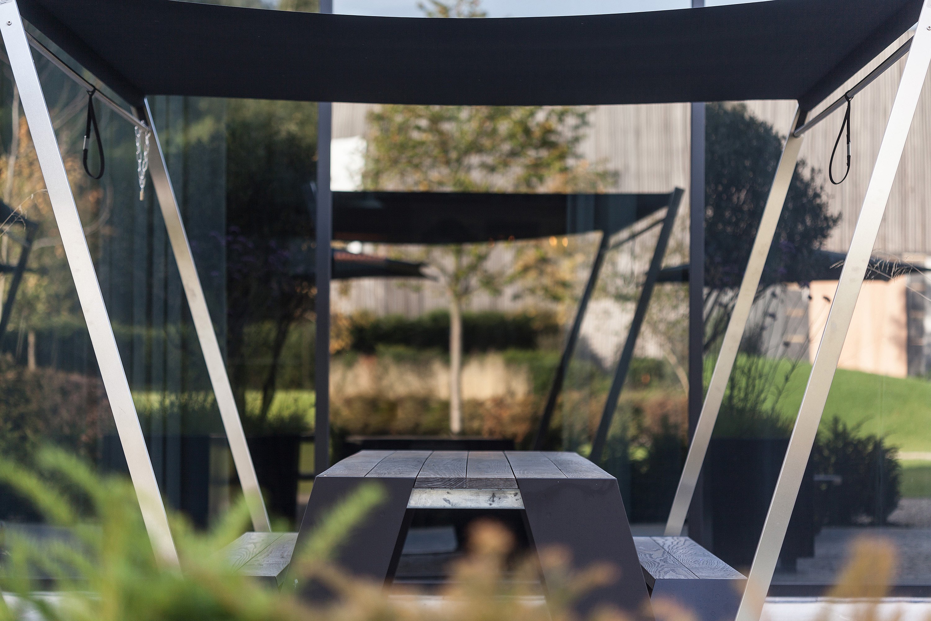 Centered view beneath a black shade toward a long black hopper, framed by angled white supports and reflected in the glass wall behind.
