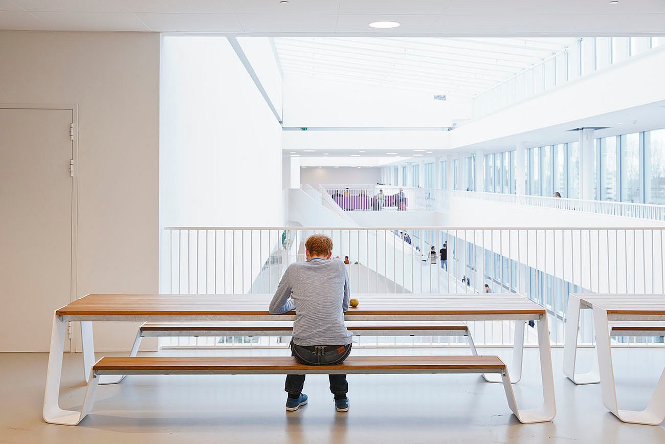   Een persoon zit alleen aan een lange Hopper picknicktafel, van achteren gezien terwijl hij uitkijkt over de grote witte hal.