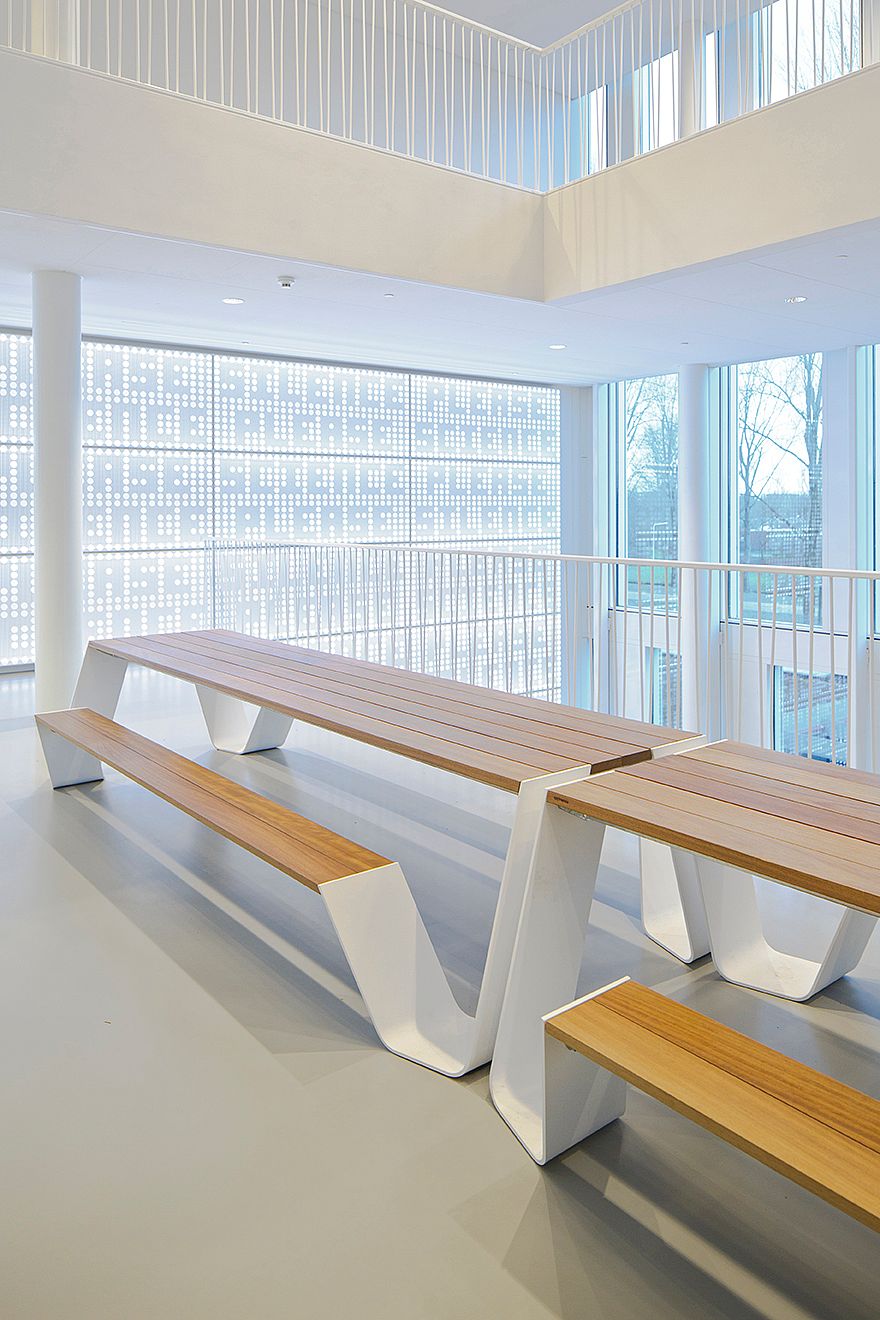 Twee witte Hopper picknicktafels met houten bladen op een bovenverdieping, tegen een geperforeerde muur die daglicht in de hal filtert.