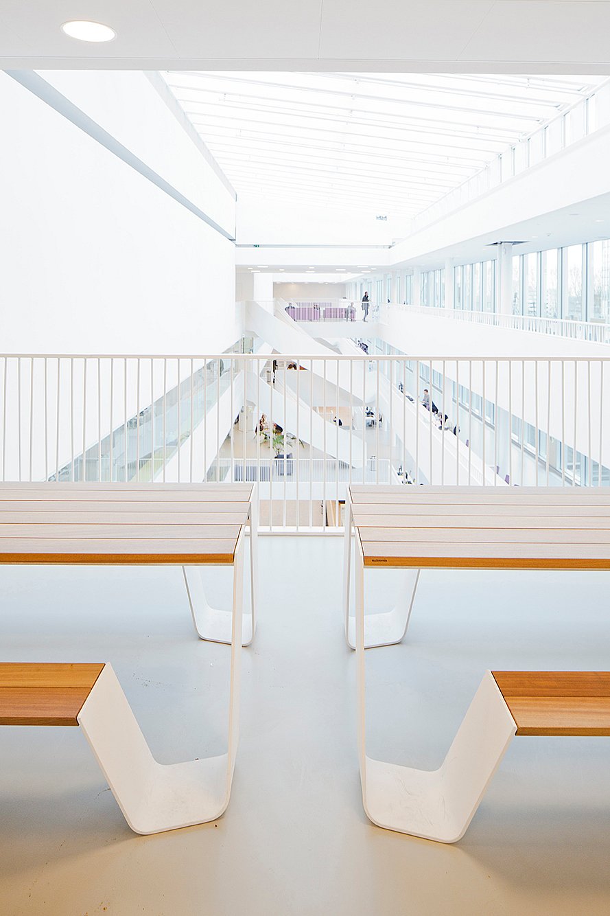   Symmetrisch zicht over de open hal met vier Hopper tafeluiteinden op de voorgrond, witte balustrades en meerdere lichte circulatieniveaus die in de verte verdwijnen.