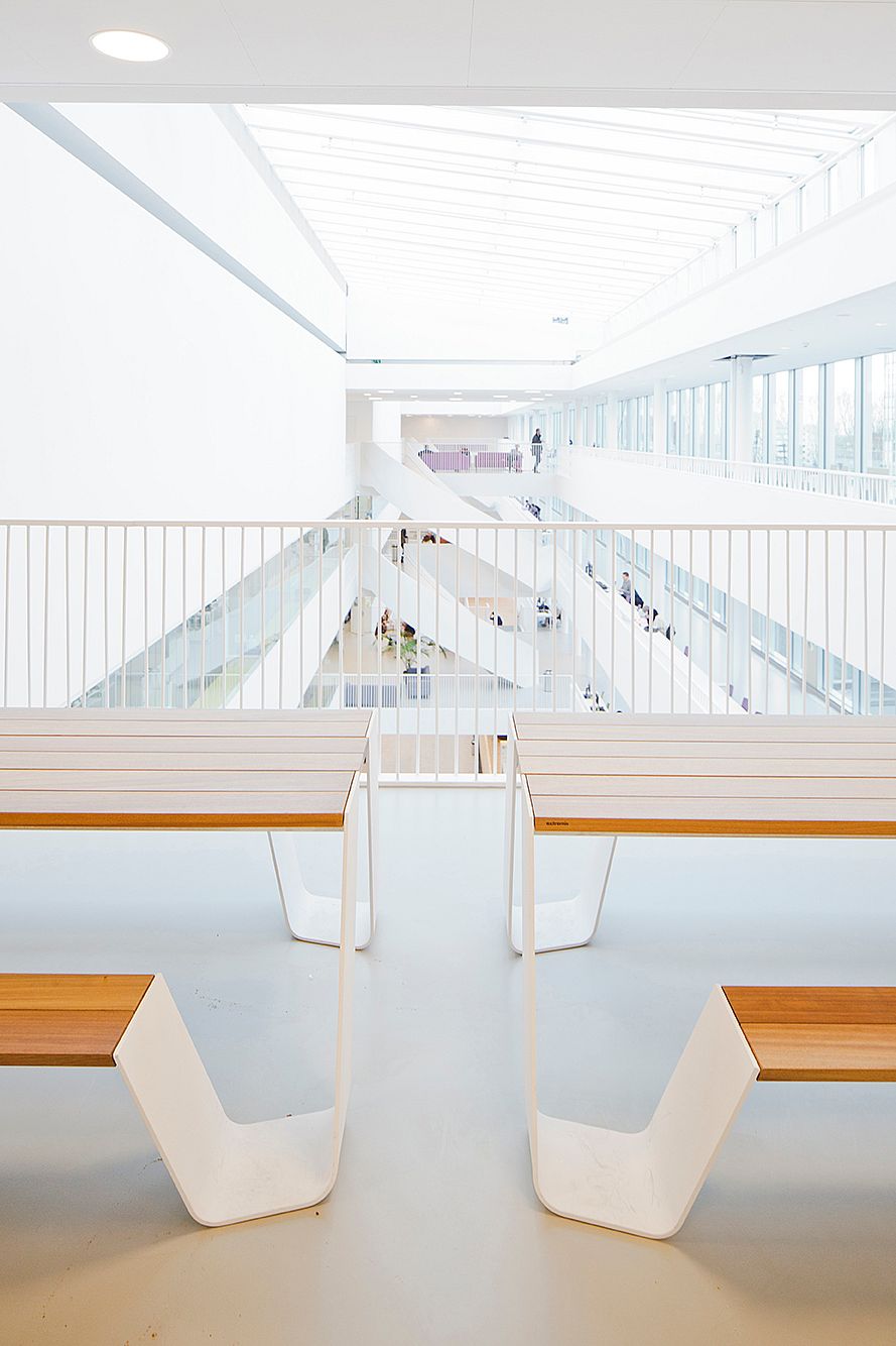 Symmetrisch zicht over de open hal met vier Hopper tafeluiteinden op de voorgrond, witte balustrades en meerdere lichte circulatieniveaus die in de verte verdwijnen.