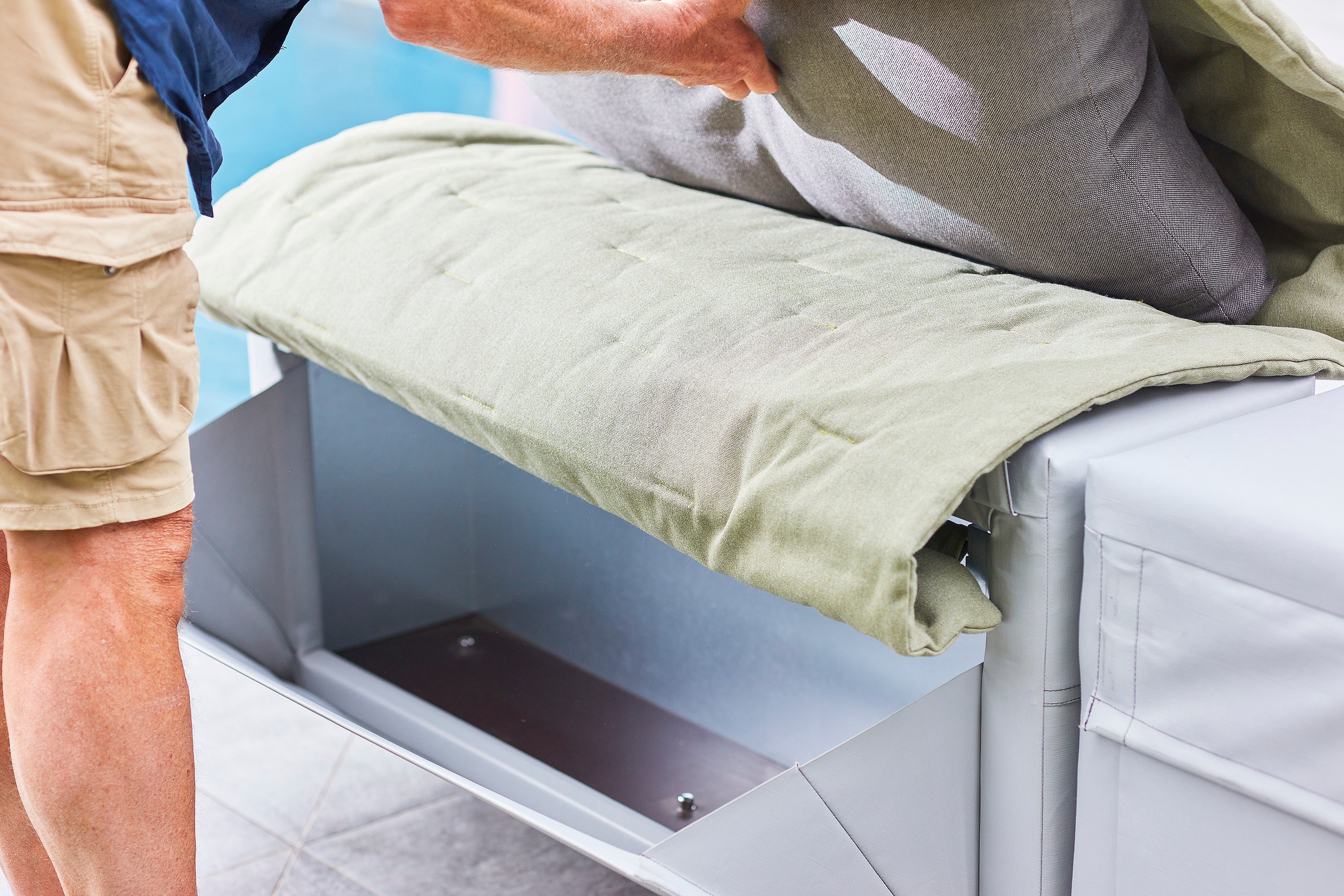 Nahaufnahme einer Person, die das Sitzkissen eines grauen Walrus-Sofas anhebt, um das darunter eingebaute Staufach freizulegen.