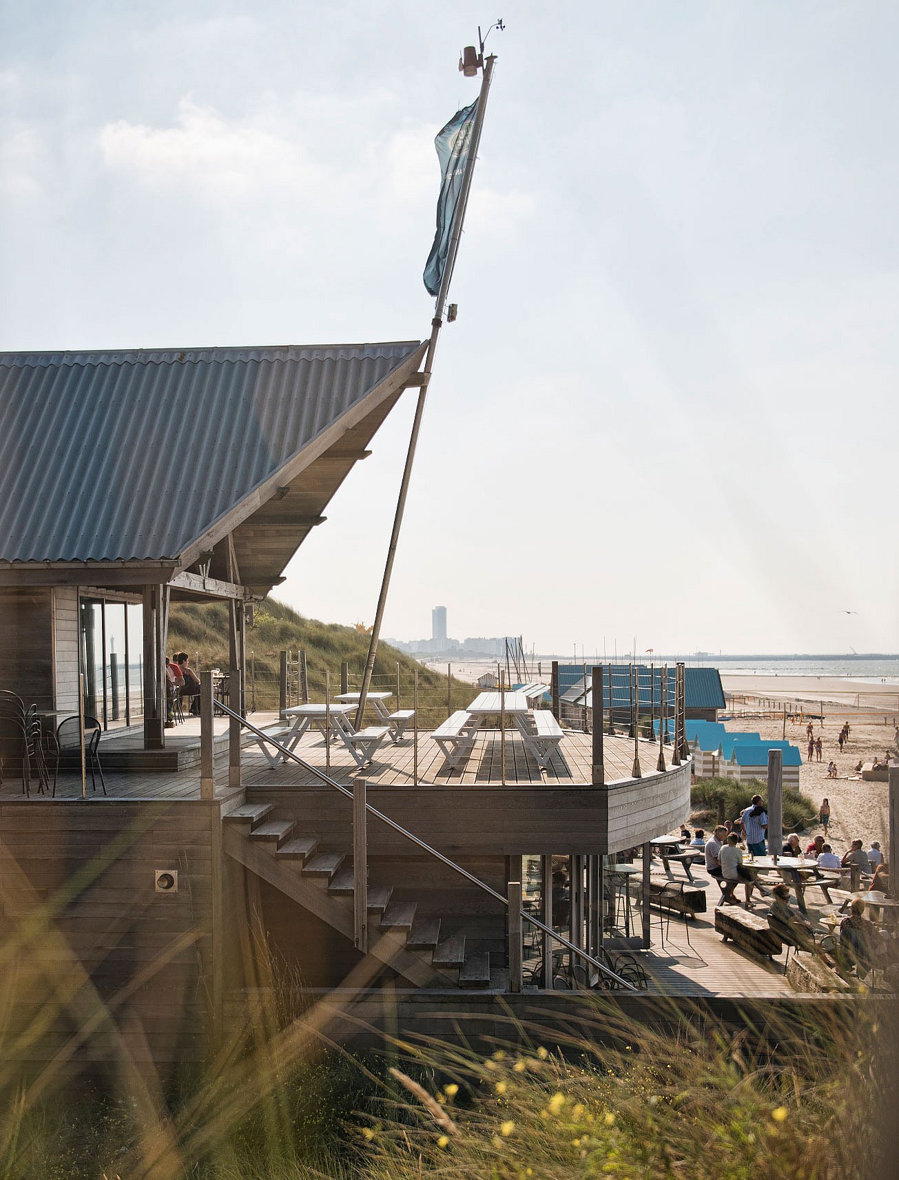Vue panoramique du bar de plage Twins en bois avec ses terrasses étagées, ses tables de pique-nique blanches, ses herbes des dunes et la plage qui s'étend à côté.