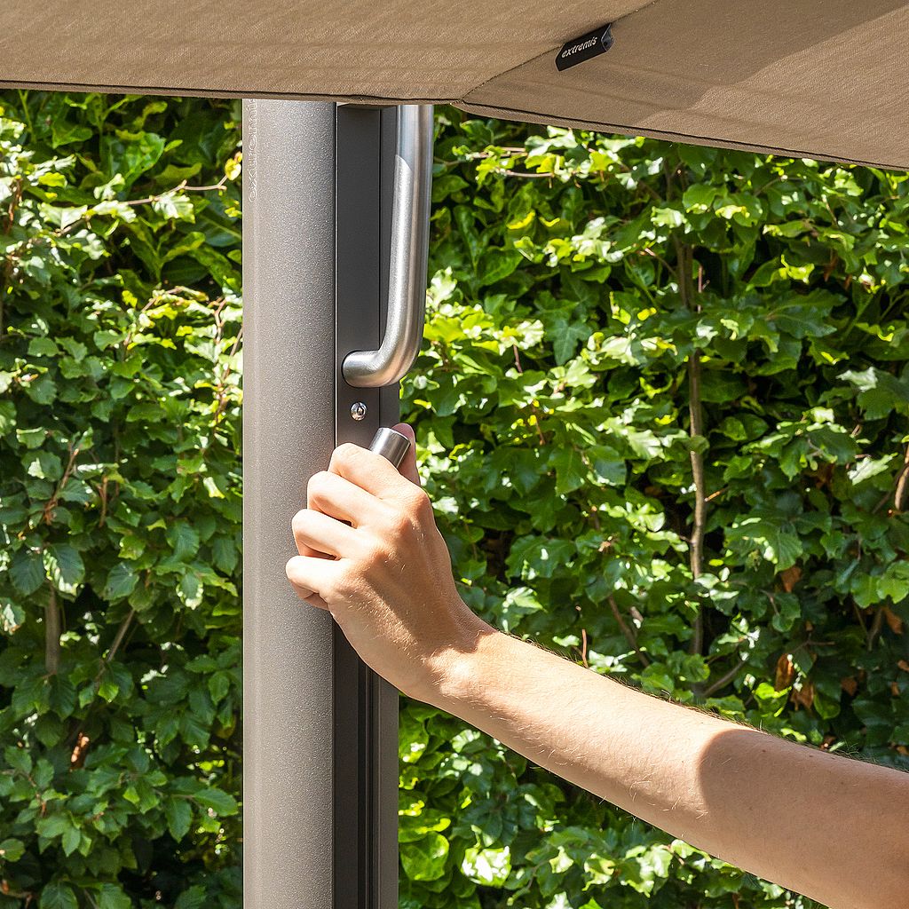 Close-up of a hand operating the handle on a Sensu parasol pole beneath the beige canopy.