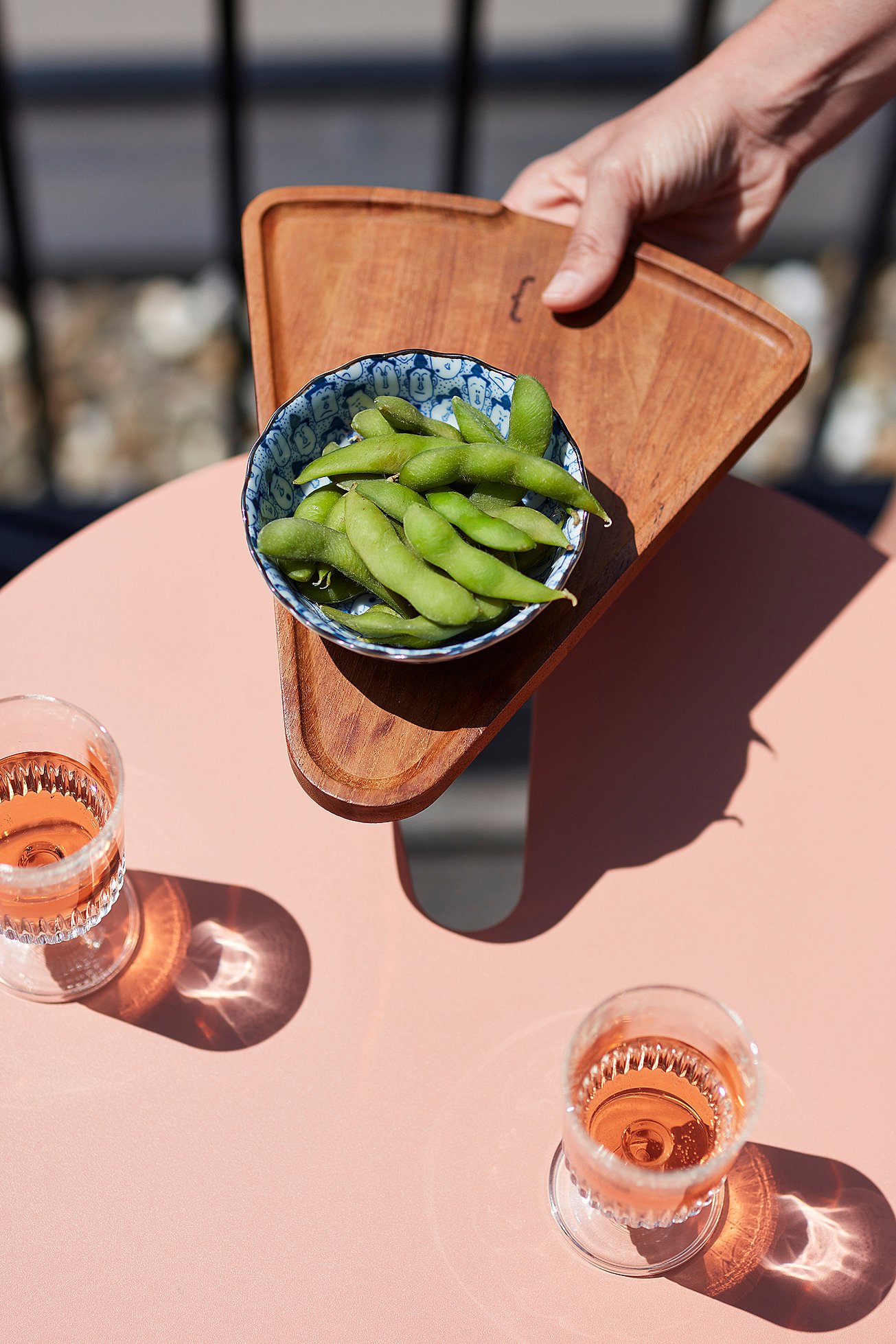 Bovenaanzicht van een koraalbalkontafel met twee glazen rosé en een houten serveerbord met een kom edamame.