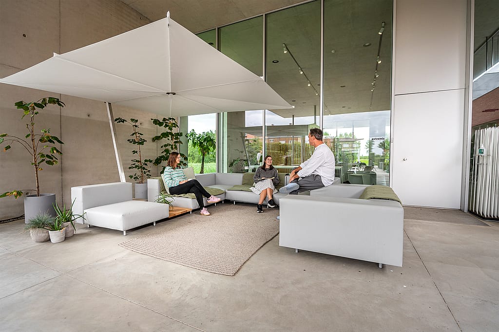 Large vue d’un walrus extérieur sous un grand parasol blanc, avec des canapés gris disposés autour d’un tapis sur une terrasse couverte.