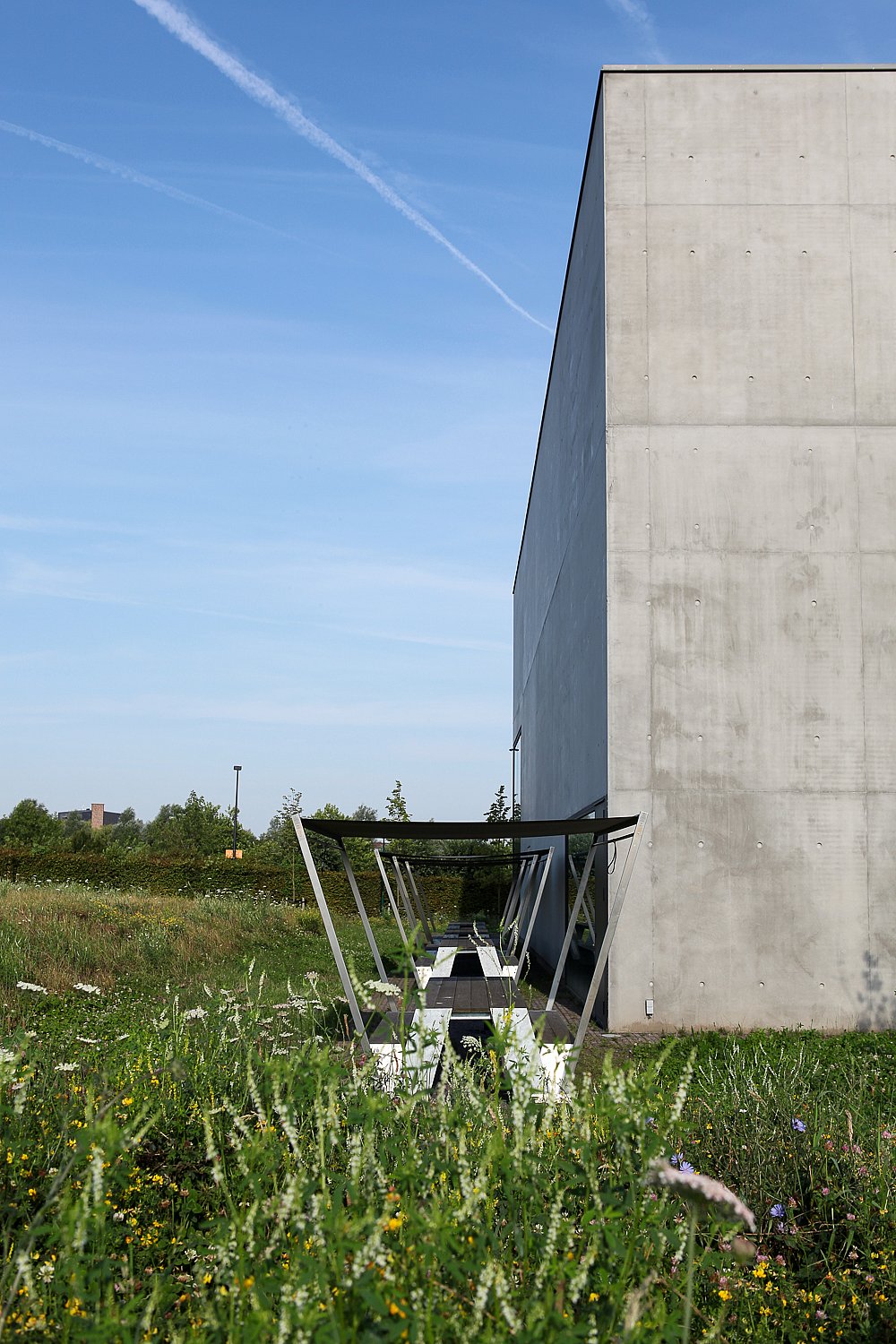   Longue table de pique-nique Hopper ombragée longe un grand bâtiment en béton, entourée d'une prairie naturelle.