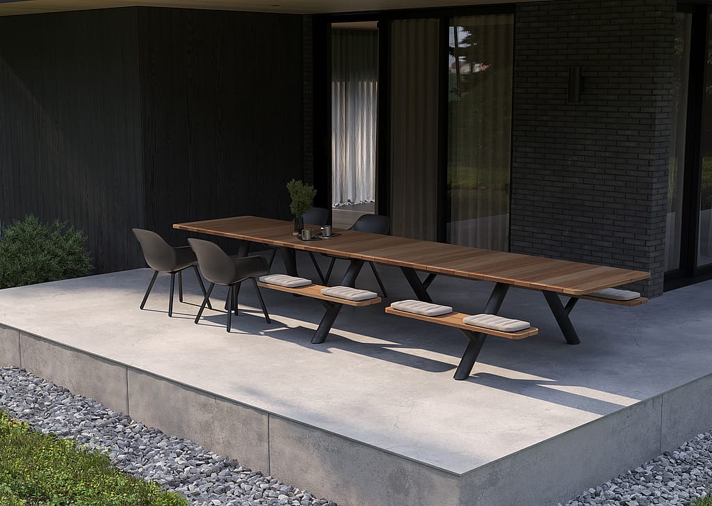 Angled view of the long Panigiri table with bench cushions and black chairs on a minimalist concrete terrace beside the house.