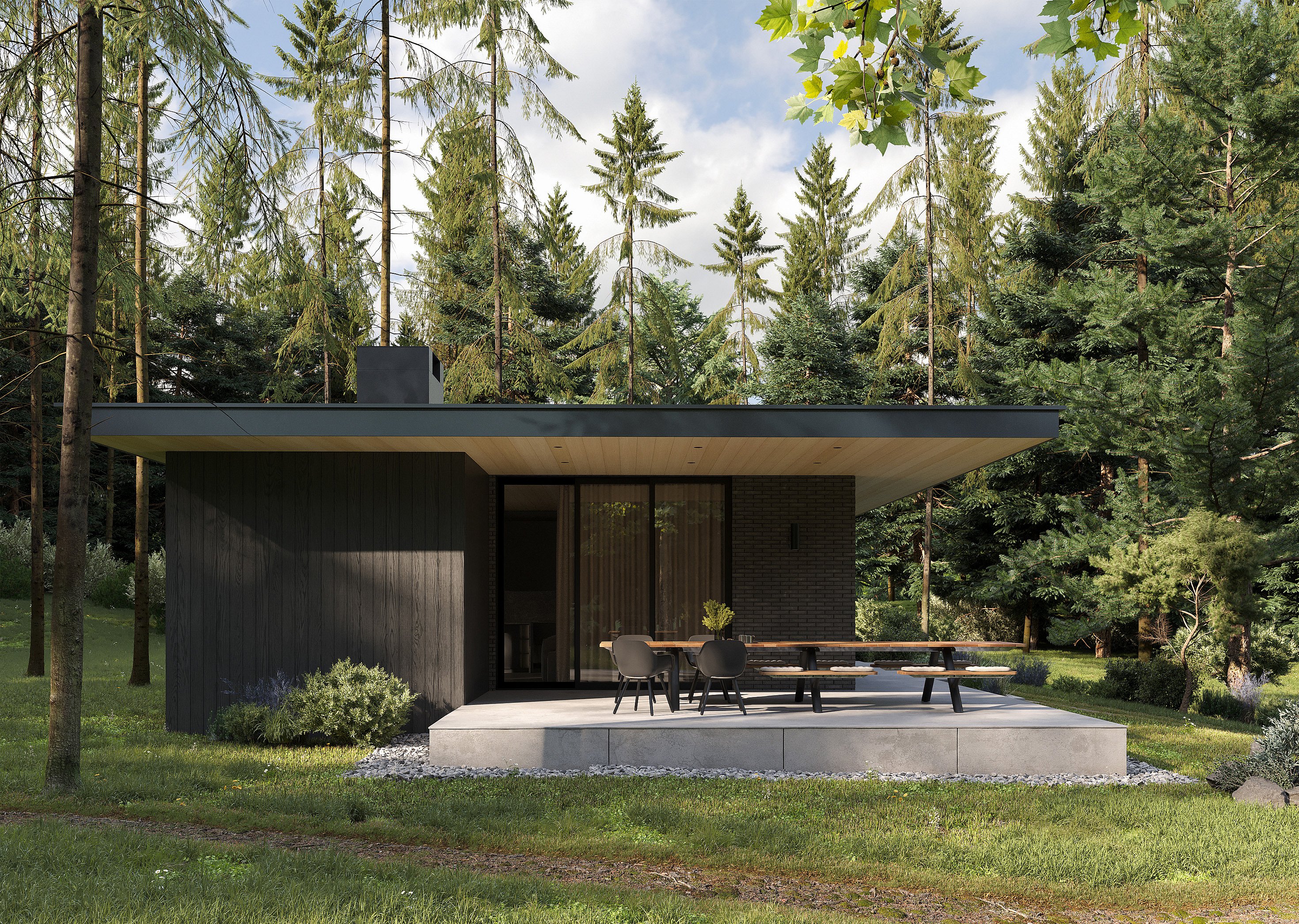 Front view of a dark modern bungalow in a forest clearing, with a long outdoor dining table and chairs on the shaded terrace.