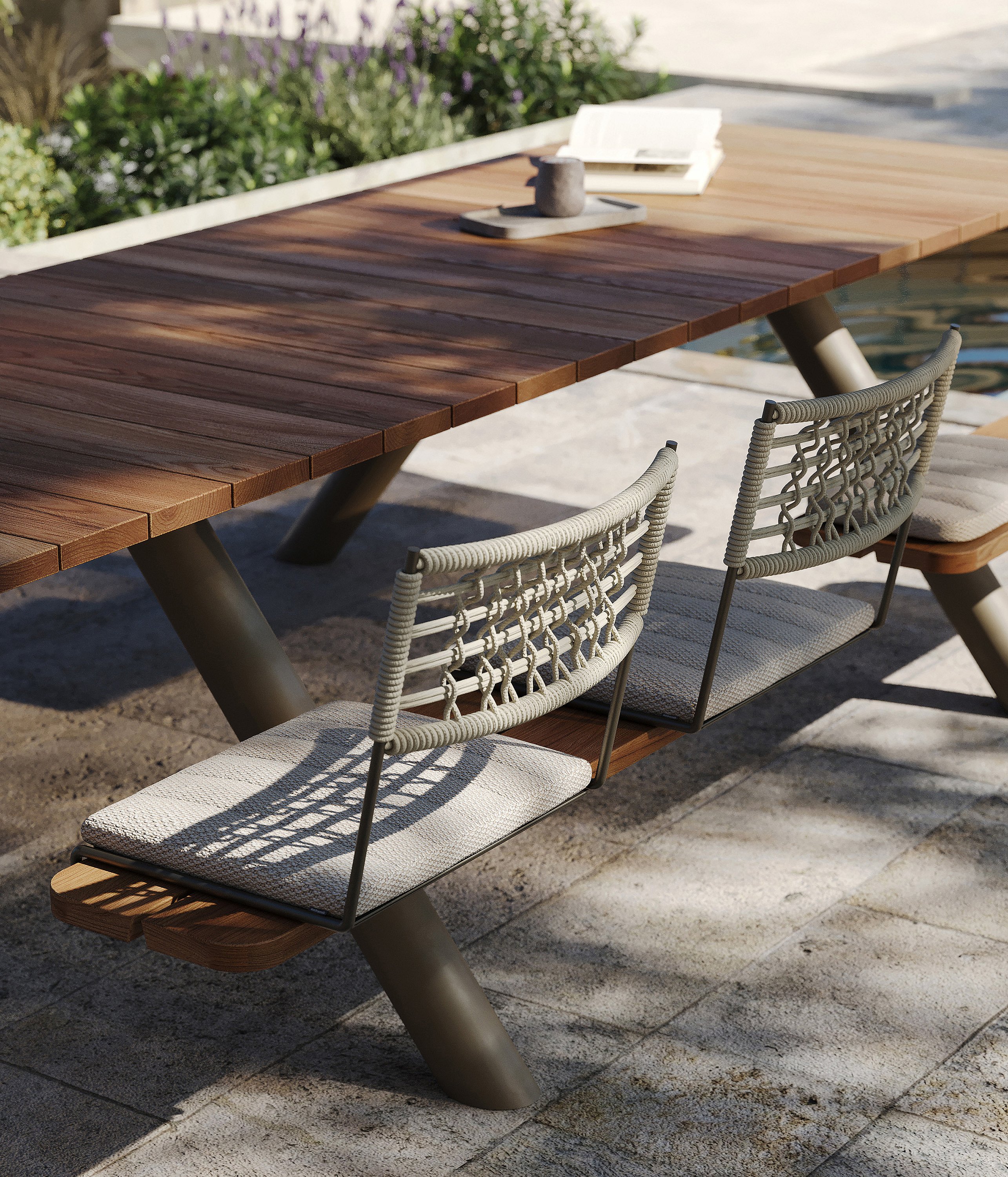 Close-up of the Panigiri wooden tabletop with woven BYOS backrests and light seat cushions beside a poolside planting bed.