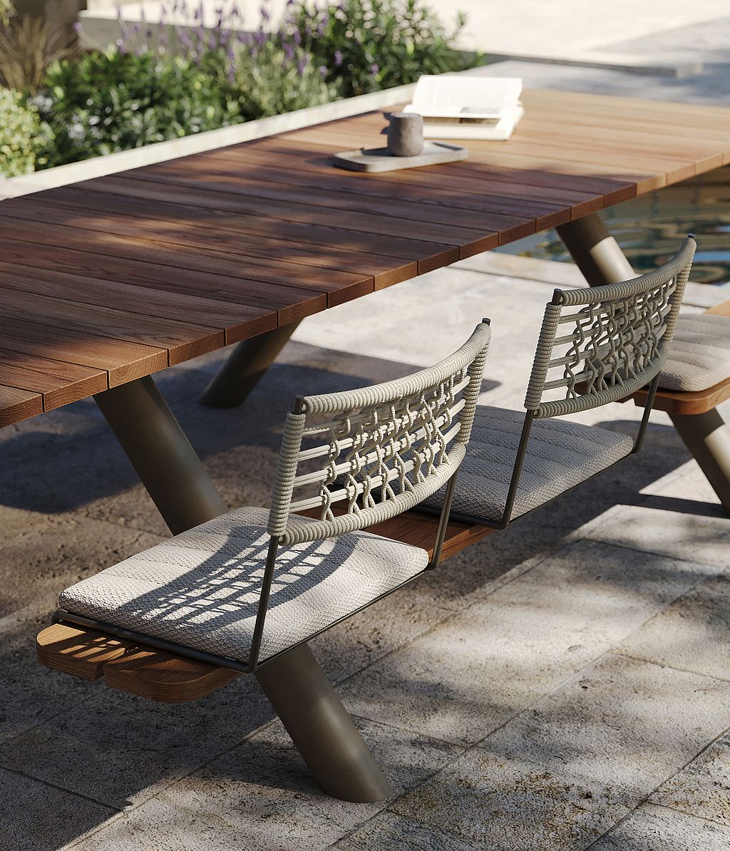 Close-up of the Panigiri wooden tabletop with woven BYOS backrests and light seat cushions beside a poolside planting bed.
